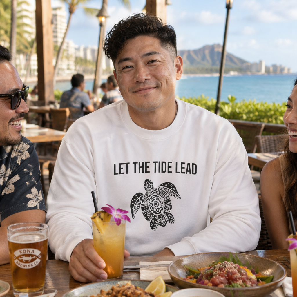 Man at a beach cafe wearing the white Let the Tide Lead turtle crewneck