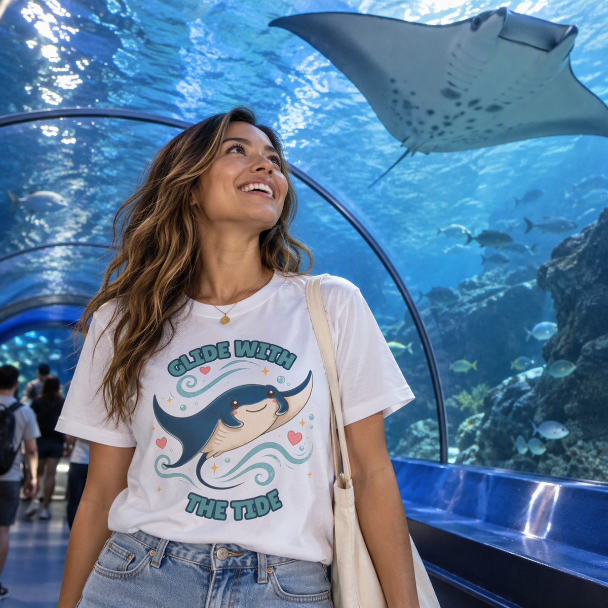 Woman in an aquarium tunnel wearing the white Glide With the Tide manta ray tee