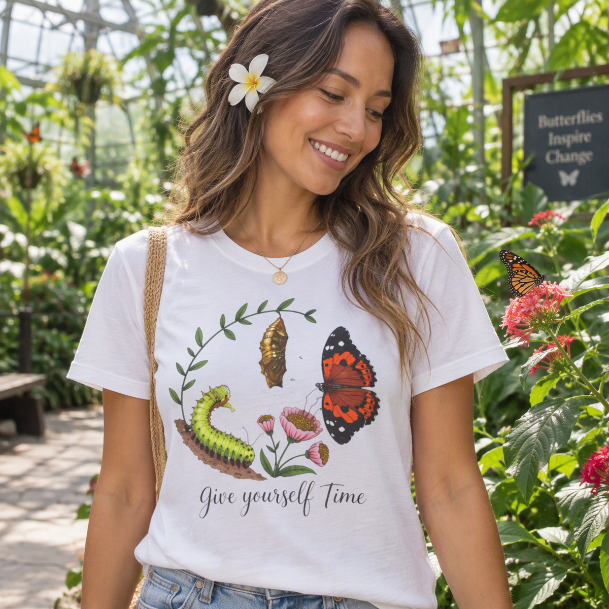 Woman standing in a garden wearing the white Give Yourself Time butterfly transformation tee