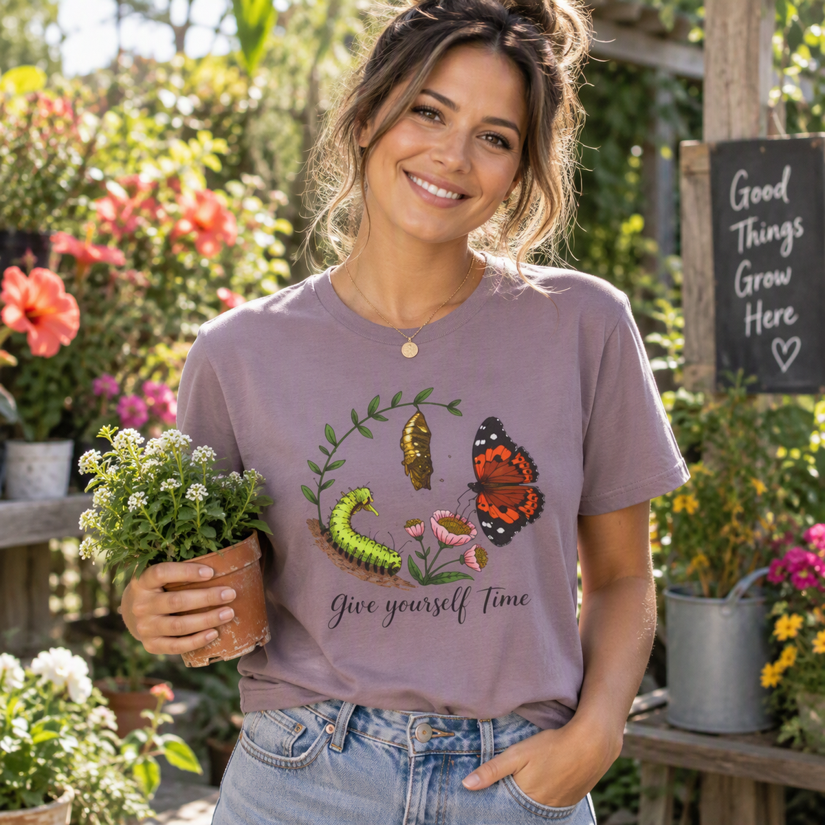 Woman holding a potted plant at a garden center wearing the paragon Give Yourself Time butterfly tee